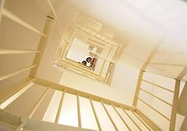 Dos vecinas, asomadas al hueco de la escalera de un edificio.