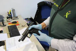 Un guardia civil de Granada muestra la pistola intervenida a los presuntos extorsionadores.