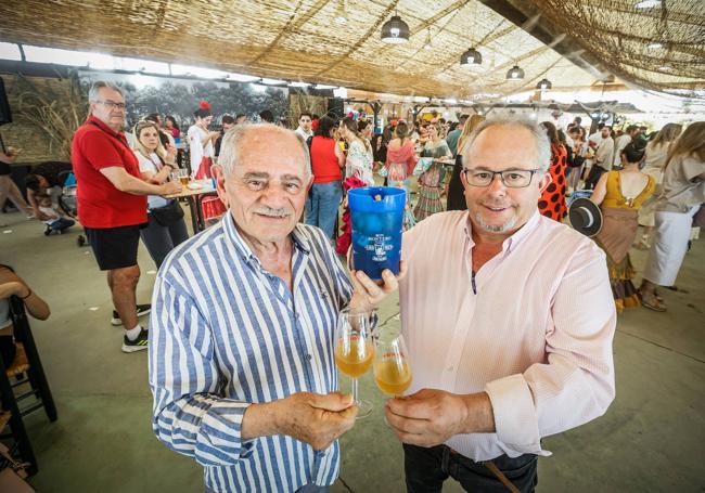 Los dos Manueles que organizan la Casa de Motril en la feria, con una jarra de Palito de ron.