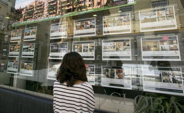 Una joven observa carteles en el escaparate de una inmobiliaria.