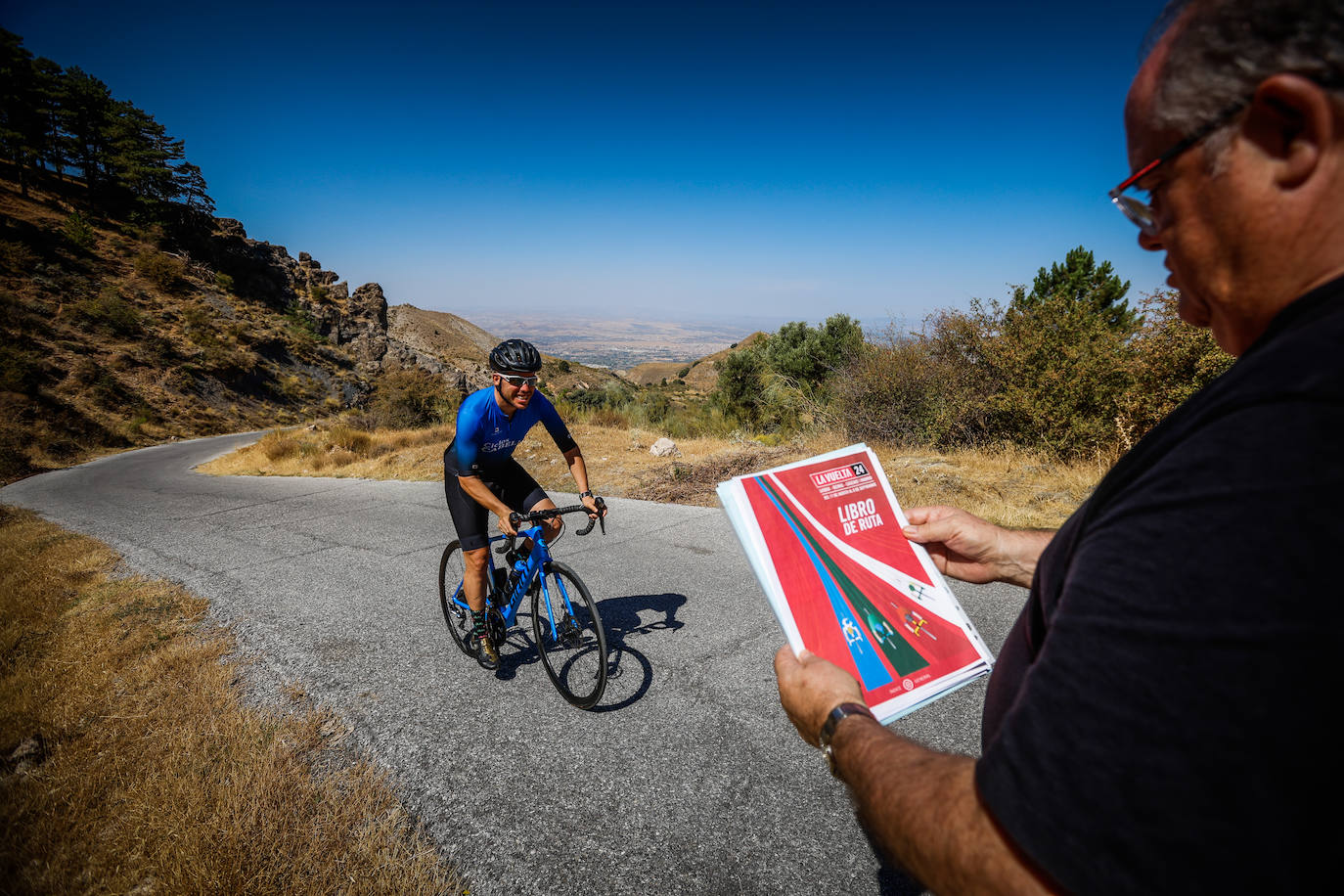 Francis Anguita sube por el Purche mientras su padre sujeta el libro de ruta de la Vuelta 2024.