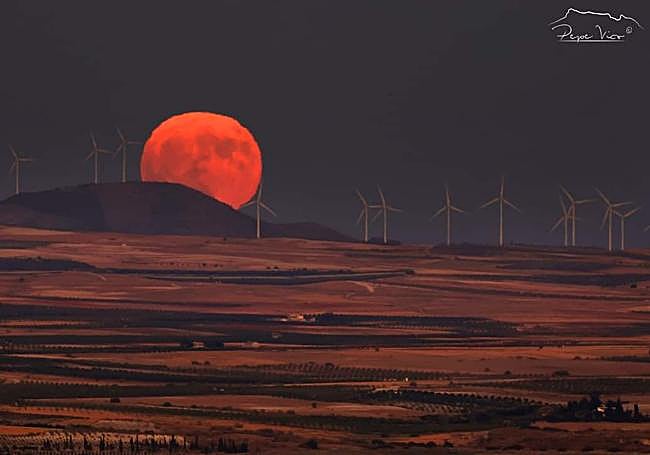 La Luna asomando entre molinos de viento.