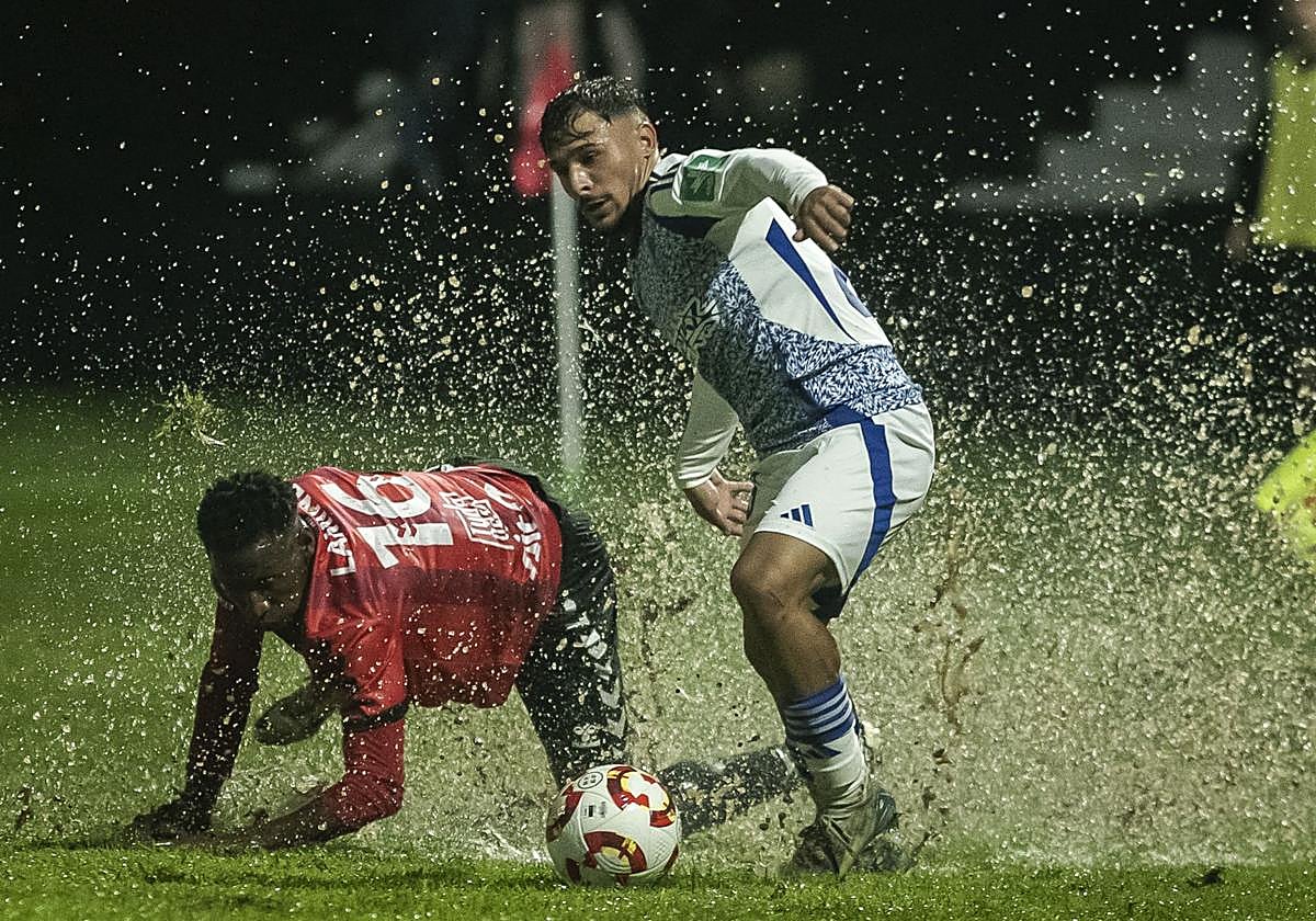 Sergio Rodelas deja atrás a un futbolista del Cortes entre charcos en Tudela.