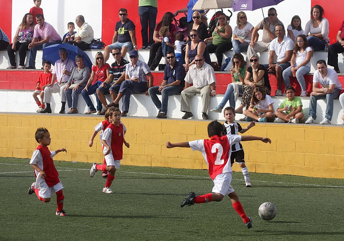Un partido de fútbol base con público en la grada.