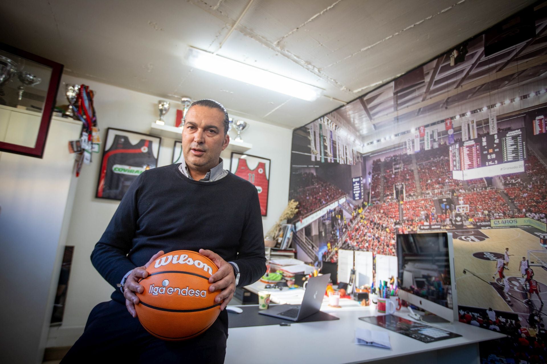 Óscar Fernández-Arenas posa en su despacho de la sede del Fundación CB Granada, con el Palacio de los Deportes abarrotado en un gran mural a la derecha.