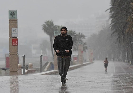 Una persona en patinete bajo la lluvia que caía ayer al mediodía en Almería.
