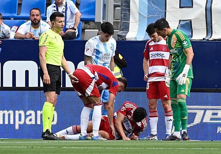 Los jugadores del Granada atienden a un dolorido Miguel Rubio en La Rosaleda.