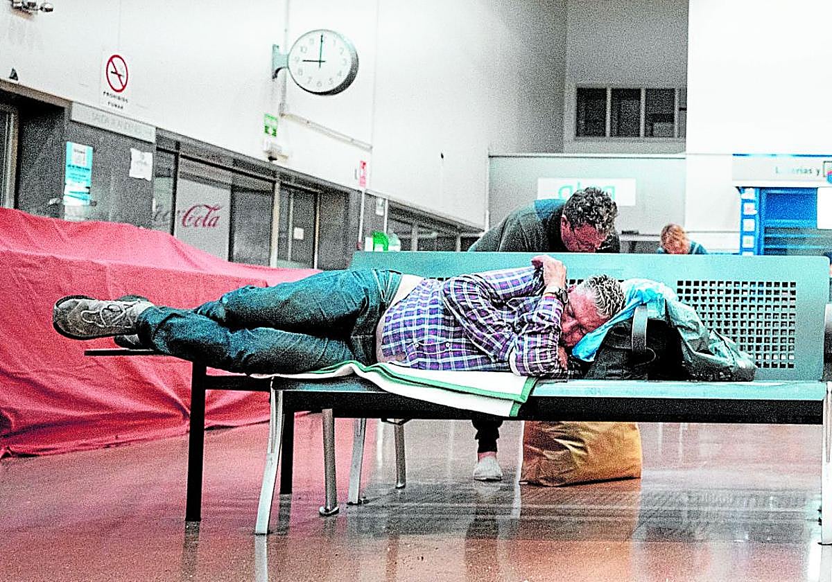 Una persona duerme recostada en la única silla que al no tener reposabrazos permite tumbarse a lo largo en el interior de la estación de autobuses de Granada.