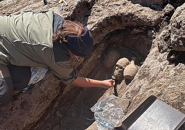 Arqueólogos excavan una de las tumbas, donde se observa un cráneo junto a una vasija.