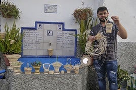 Enrique Carmona mostrando algunos de sus objetos en miniatura tejidos con fibra junto al pilar de la Placeta de Santa Ana