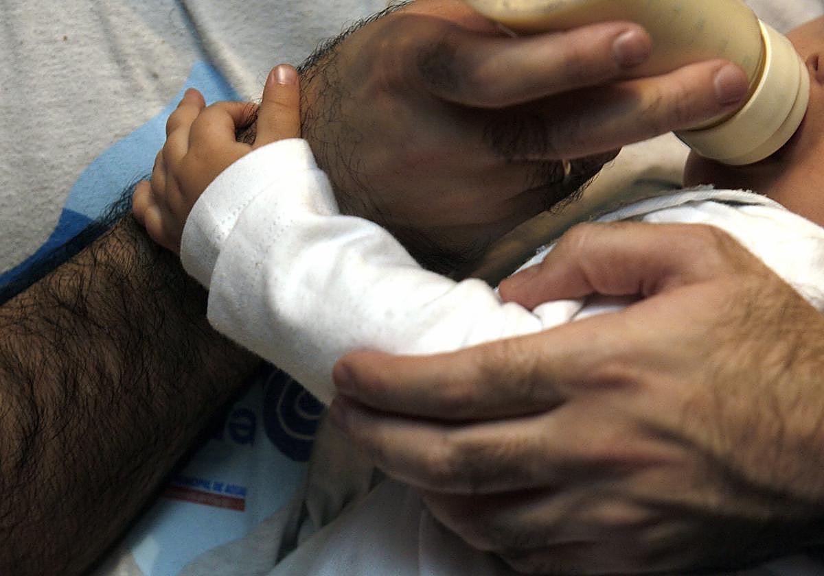 Un hombre da el biberón a su hijo.