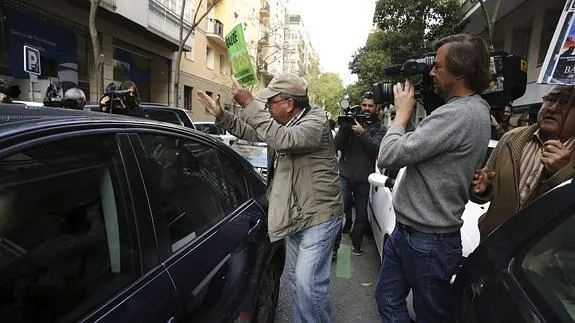 Un preferentista de Bankia junto al coche en el que viaja Rato. 