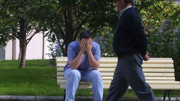 Un joven sentado en un banco se tapa la cara con las manos.