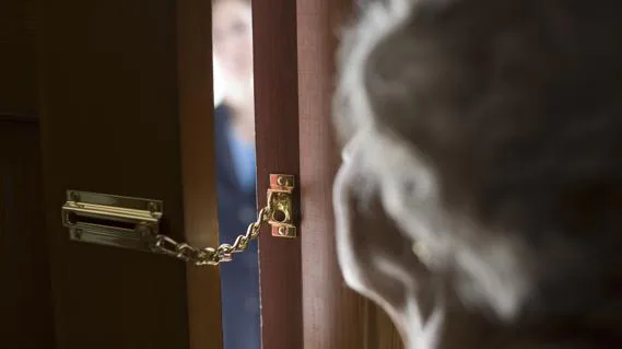 Anciana abre la puerta de su casa con la cadena de seguridad puesta. 
