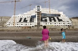 Una mujer y dos niños, en la playa de El Algarrobico, en Carboneras, con el hotel de Azata del Sol al fondo. /IDEAL