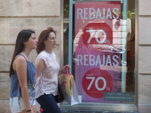 Una chica con una bolsa de compras pasa frente a un escaparate en rebajas.