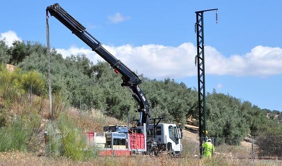 Un camión grúa descarga los postes que sujetarán la catenaria del AVE en el barrio lojeño de La Esperanza.