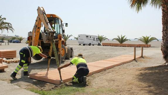 Dos operarios instalan una pasarela de hormigón en la playa motrileña del Cable.  