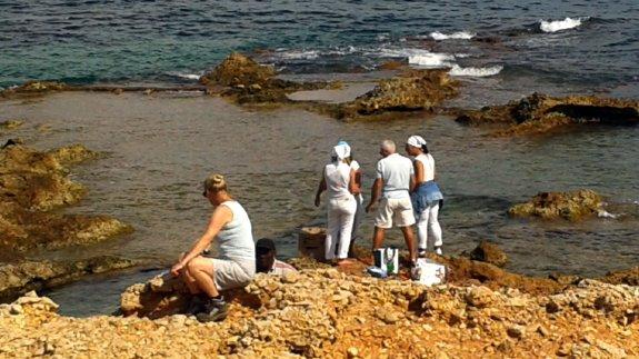 Una turista se interesa por el ritual mientras los participantes charlan tras acabar la ceremonia en la playa de Les Rotes.
