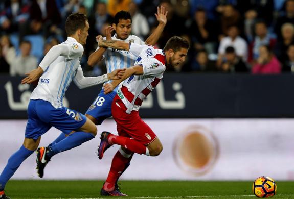 El delantero ucraniano del Granada Artem Kravets (d), lucha por el balón ante los defensas del Málaga, Diego Llorente (i) y el venezolano Roberto Rosales.