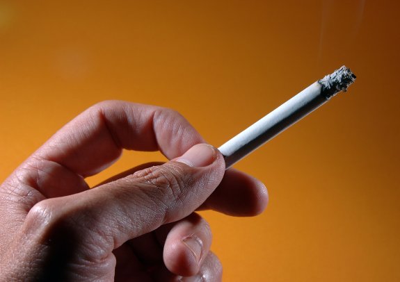 Un fumador sostiene en su mano un cigarrillo encendido.