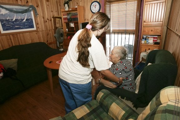 Una auxiliar ayuda a levantarse a una usuaria de la ayuda a domicilio.