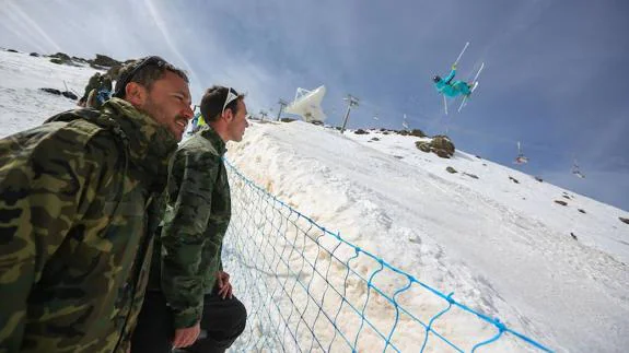 Dos militares observan junto a la pista de la Visera el entrenamiento de un participante de freestyle ski en estos campeonatos de Sierra Nevada.