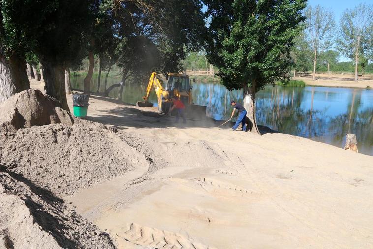 Operarios y máquinas extienden la arena en la playa situada en la zona del campo de fútbol y el chiringuito.