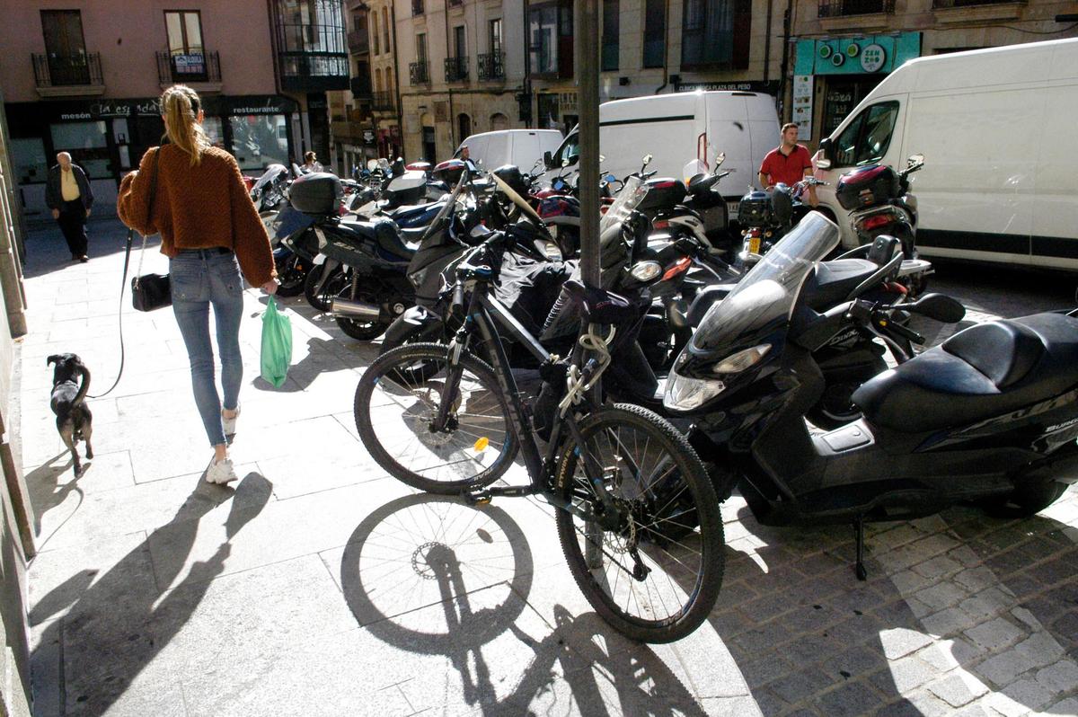 Una bicicleta aparcada en una acera junto a una zona de estacionamiento para motos.