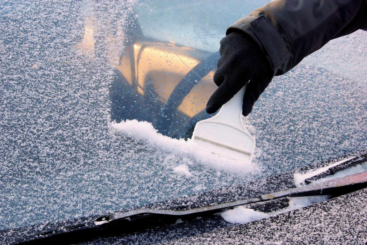 Un conductor retirar el hielo de la luna con una rasqueta.