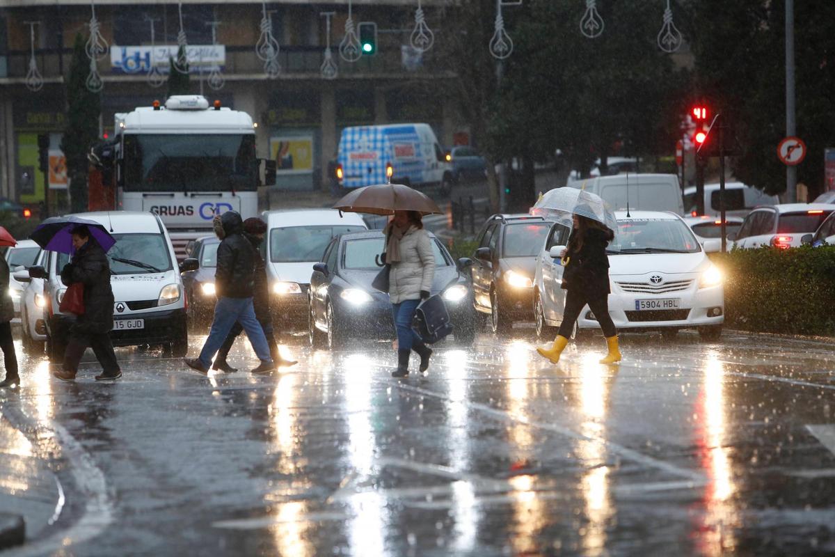 Varias personas tratan de refugiarse de la lluvia con paraguas en Salamanca.