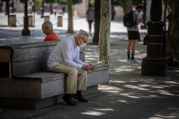 Un hombre con mascarilla lee el periódico sentado en un parque extremeño.