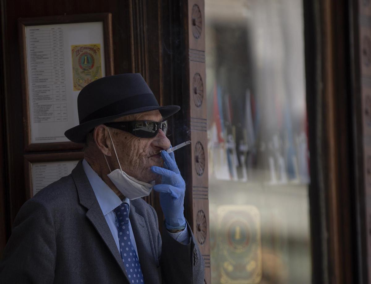 Un hombre con mascarilla y guantes fumando un cigarro.