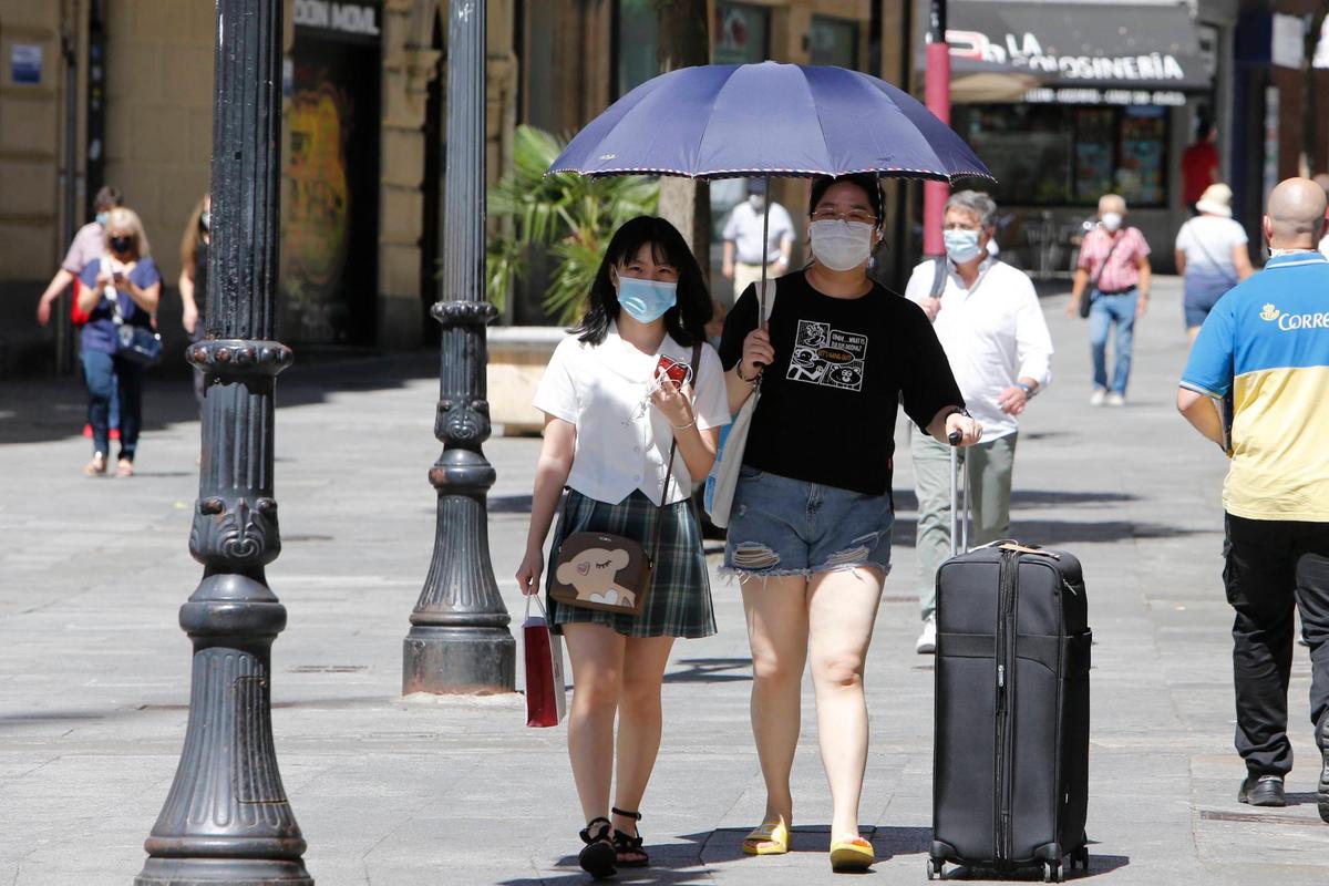 Dos turistas se protegen del calor con un paraguas en una de las calles de la ciudad