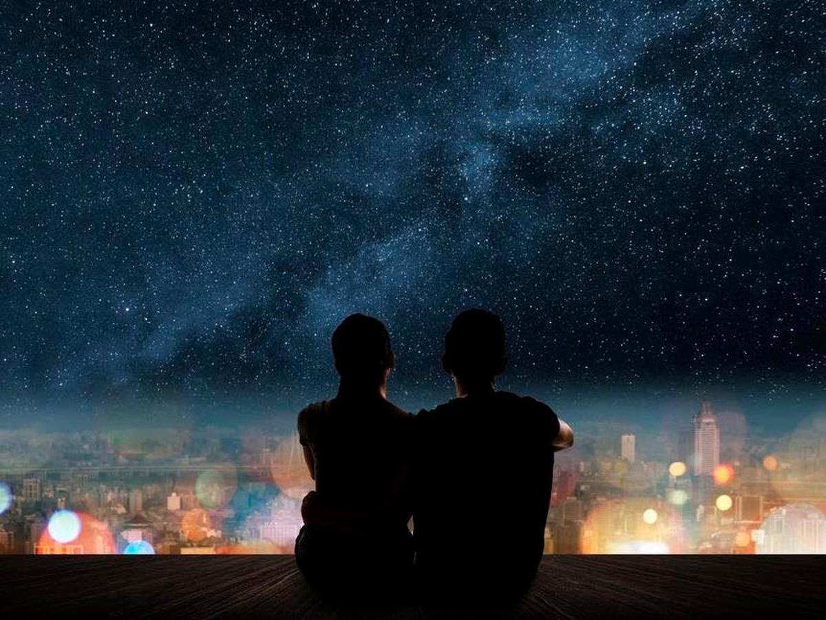 Imagen de dos personas con el cielo lleno de estrellas al fondo.