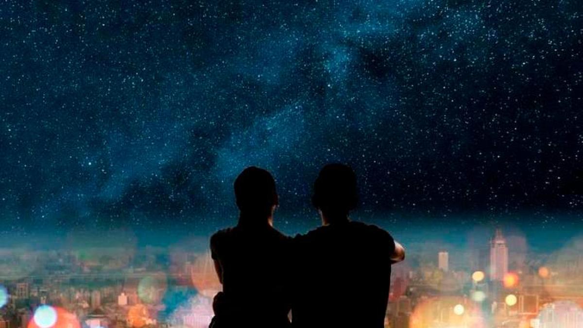 Imagen de dos personas con el cielo lleno de estrellas al fondo.