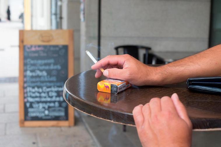 Una persona fumando a la puerta de un bar.