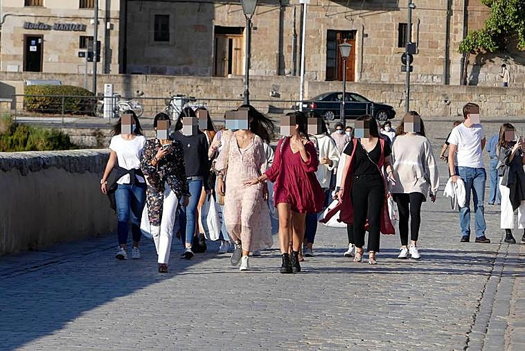 Un grupo de jóvenes, este miércoles cruzando el Puente Romano cargando con bolsas.