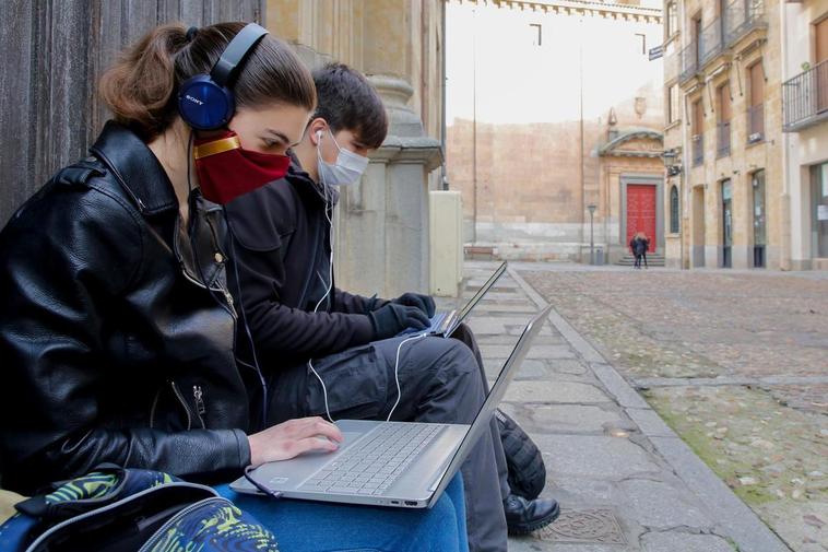 Dos jóvenes consultando internet en sus ordenadores portátiles.