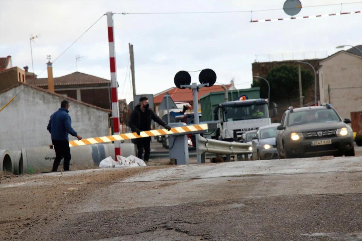 El maquinista y otra personas retiran una de las barreras averiadas del paso a nivel de acceso al casco urbano de Gomecello mientras los coches y el tren esperan.