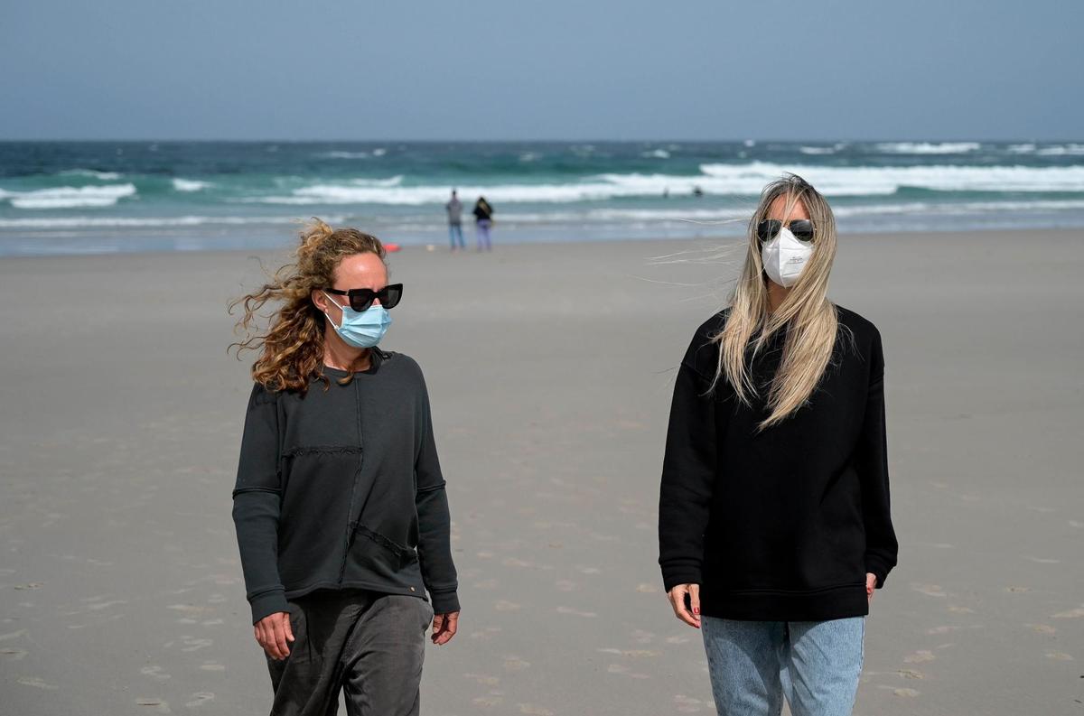 Dos chicas con mascarilla en la playa.