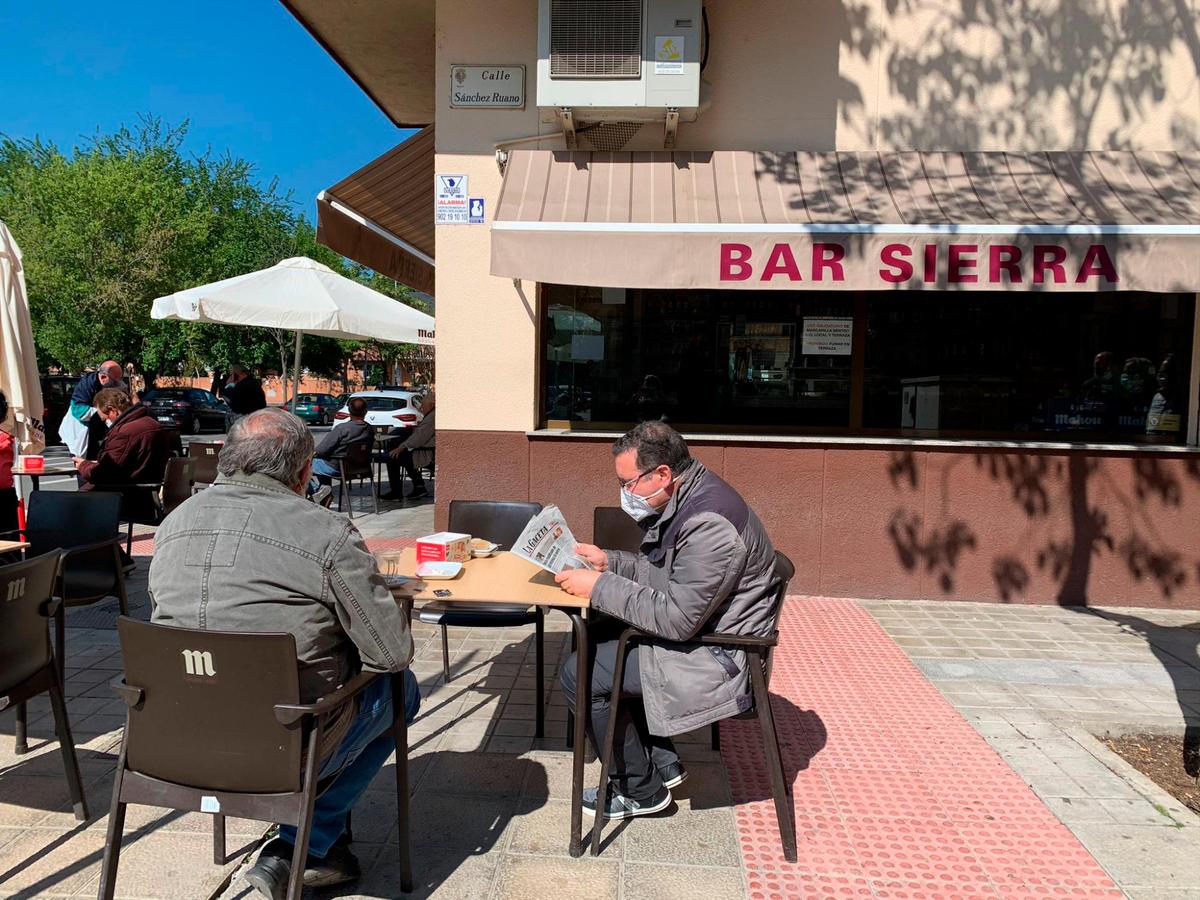 Varios clientes toman algo en una terraza mientras leen el periódico.