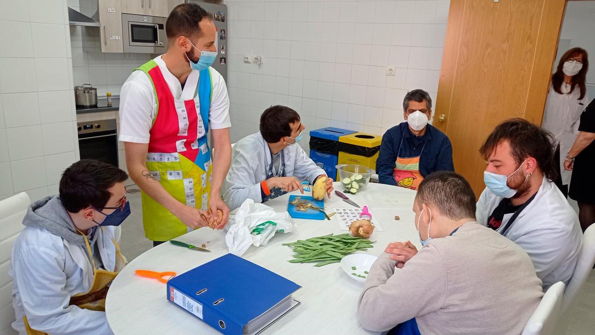 Cuatro adultos con autismo, con ayuda de dos profesionales, elaboran una receta en el taller de cocina.