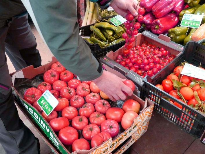 Un frutero muestra tomates de variedad rosa y un racimo de cherrys en su establecimiento