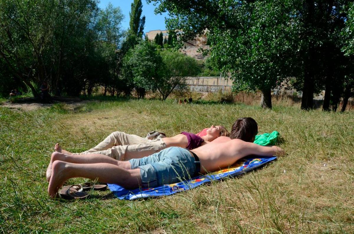 Dos jóvenes toman el sol en la ribera del Tormes a su paso por Salamanca.