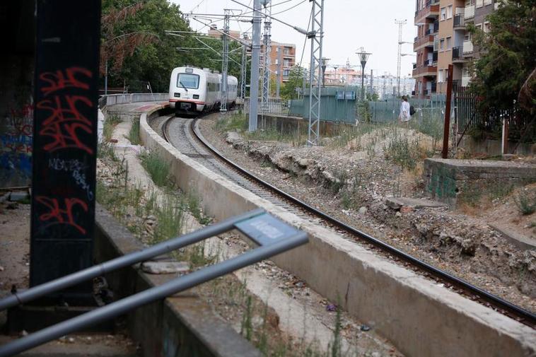 Un tren Media Distancia llegando al destartalado apeadero de la Alamedilla, mientras una mujer (derecha) atraviesa entre escombros para llegar hasta las vías.