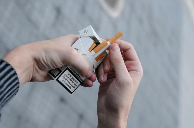 Una persona sacando un cigarro de una cajetilla.