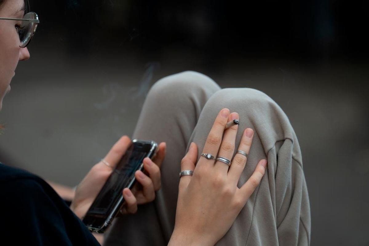 Una joven fuma un cigarro mientras observa su teléfono.