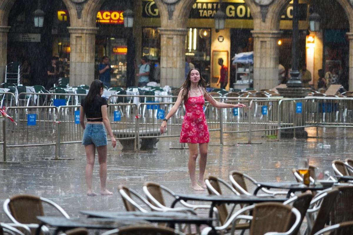 Dos chicas bailan bajo la lluvia en la Plaza Mayor.