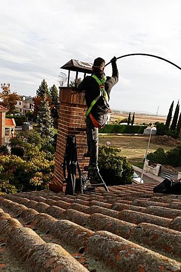 Un deshollinador desprende el hollín del interior de una chimenea en una vivienda de la Urbanización Valdelagua, en Santa Marta.